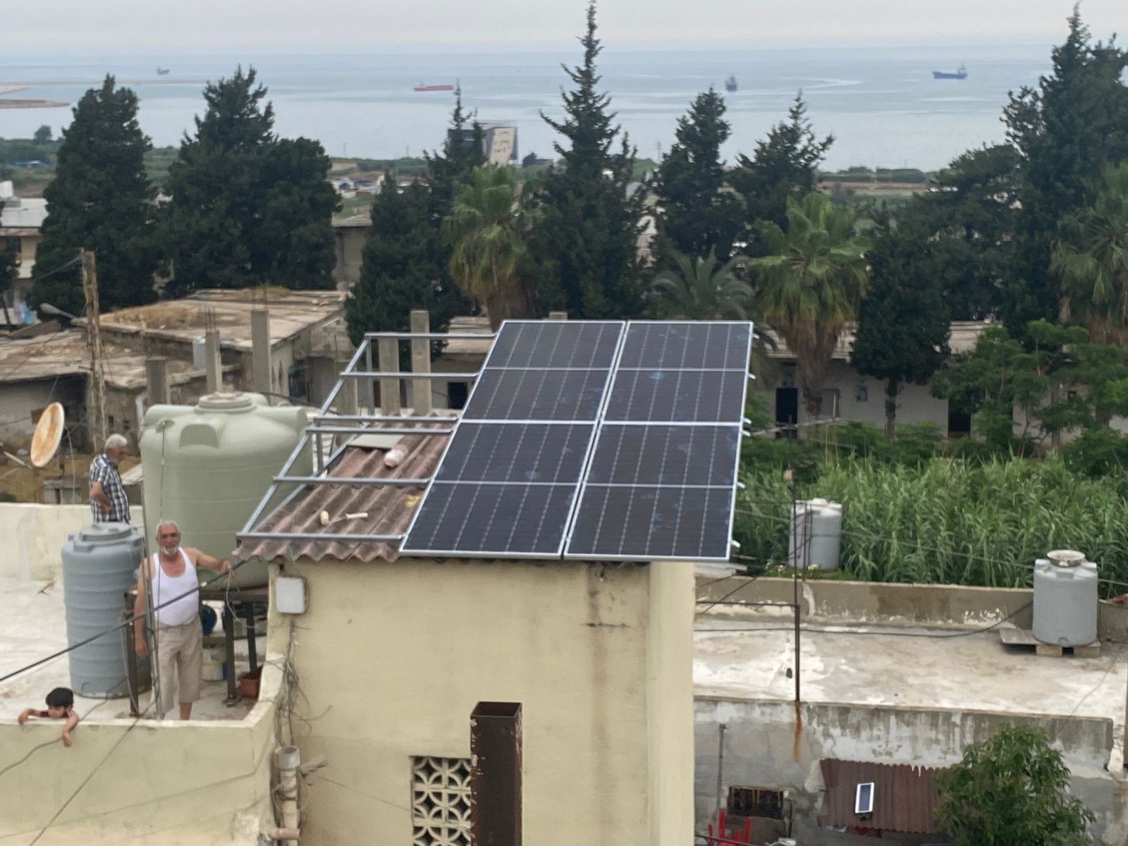 Four solar panels installed on a household rooftop beside water tanks in Lebanon
